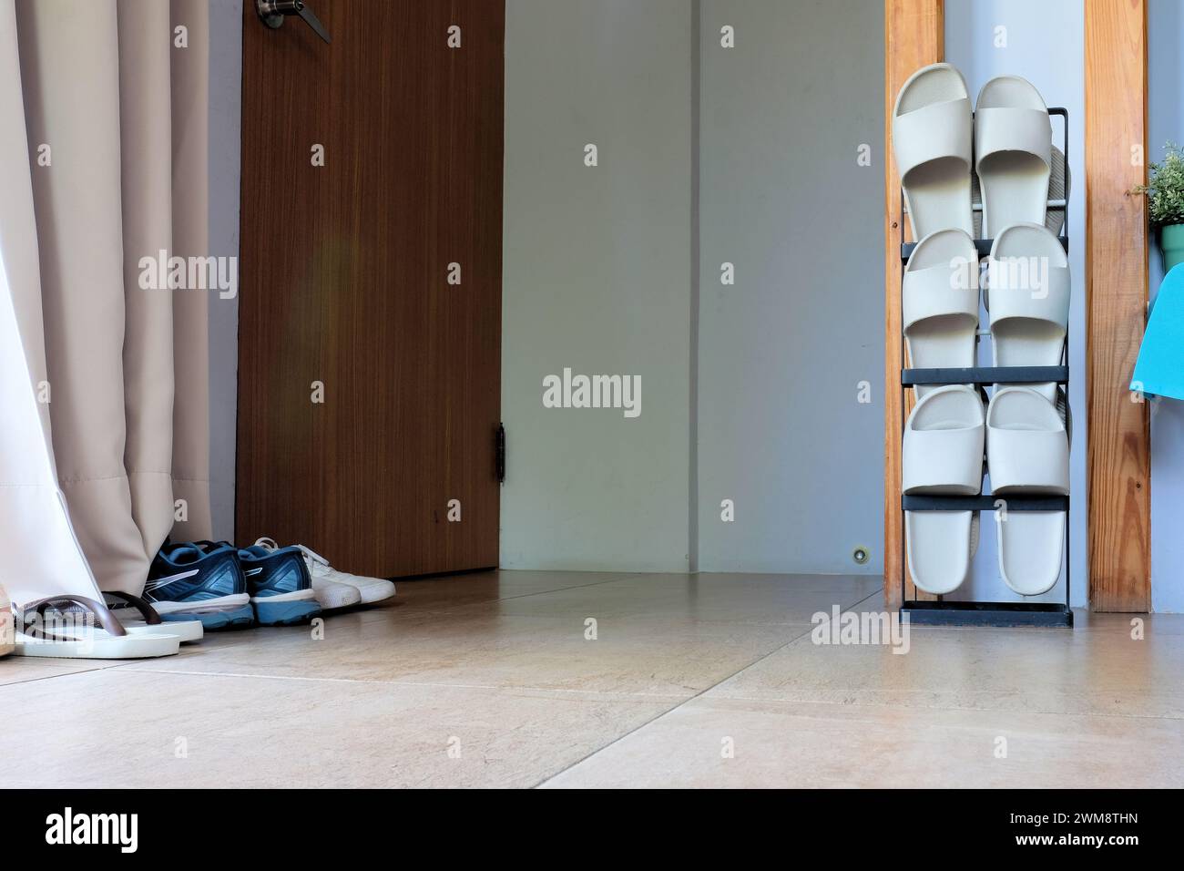 Porte-chaussures vertical contenant trois paires de sandales en caoutchouc pour une utilisation à l'intérieur situé à côté de la porte et de l'entrée avec des chaussures d'extérieur sur le sol ; Asie, Taiwan. Banque D'Images