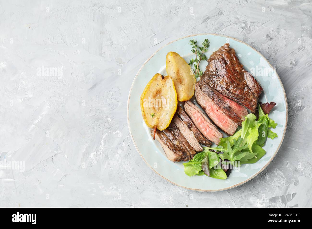 Morceaux de délicieuse viande de bœuf rôtie, poire caramélisée et légumes verts sur une table texturée légère, vue de dessus. Espace pour le texte Banque D'Images