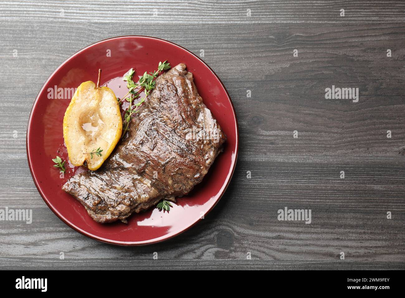 Délicieuse viande de bœuf rôtie, poire caramélisée et thym sur table en bois gris, vue de dessus. Espace pour le texte Banque D'Images