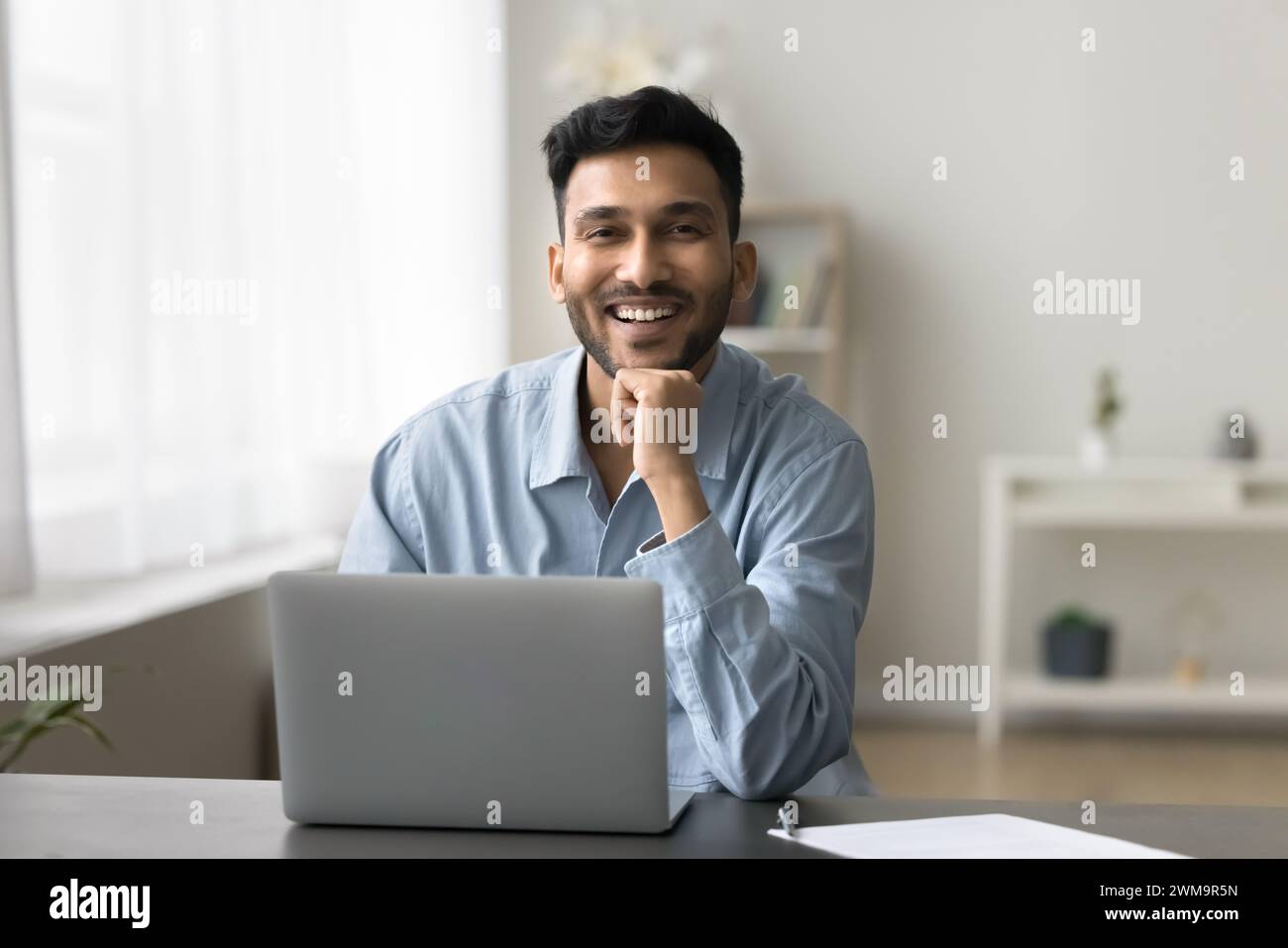 Homme indien assis à son bureau avec son ordinateur portable regardant la caméra Banque D'Images