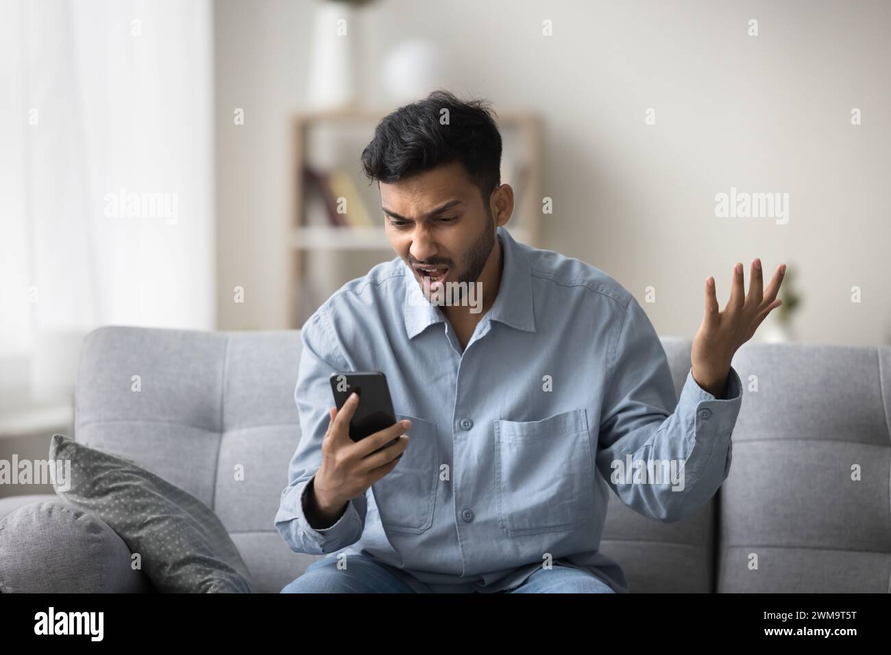 Gars indien regardant l'écran du smartphone avec l'expression du visage en colère Banque D'Images