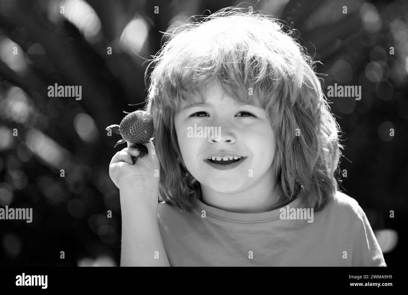 Enfant avec visage heureux manger fraise. Garde d'enfants de la paille. Banque D'Images