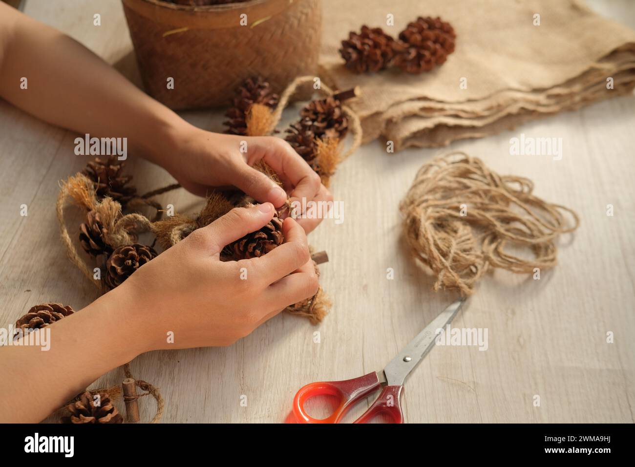 Les mains des femmes fabriquent des décorations murales à partir de pommes de pin et de corde de jute Banque D'Images