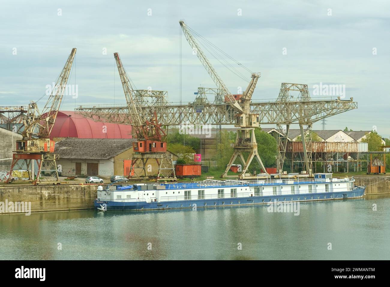 Saint-Marseille, France, 28 avril 2023 : une barge bleue flotte sur une rivière calme, amarrée dans un port industriel. Derrière elle, de grandes grues métalliques et wa Banque D'Images