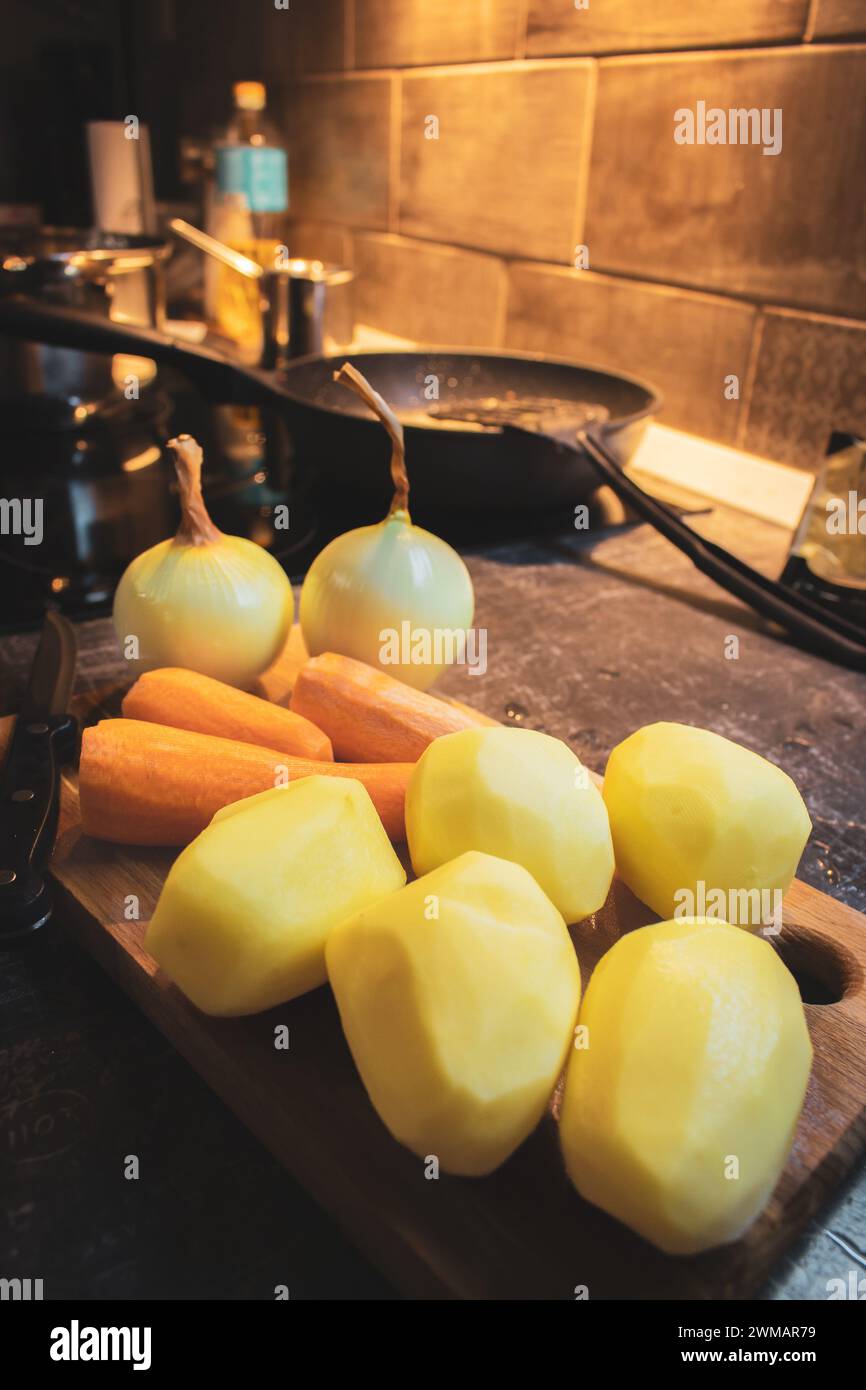 Légumes pelés sur planche de bois avec couteau. Pommes de terre crues, oignons et carottes sur la table de la cuisine. Concept de préparation des aliments. Légumes sur planche à découper. Banque D'Images