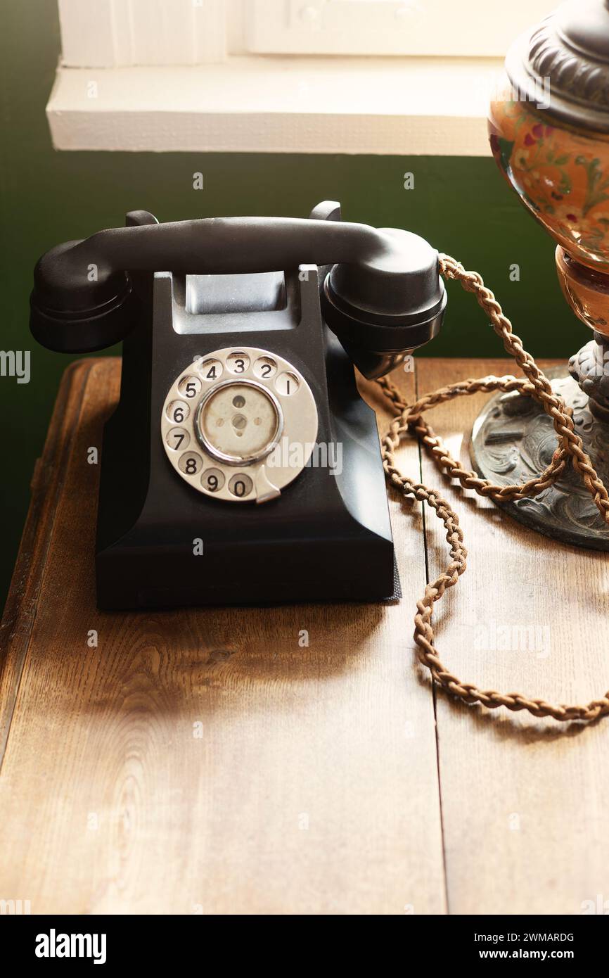 Noir, téléphone bakélite vintage des années 1940 sur un bureau en bois près de la fenêtre, table brune comme fond offrant un espace de copie vers le bas. Banque D'Images