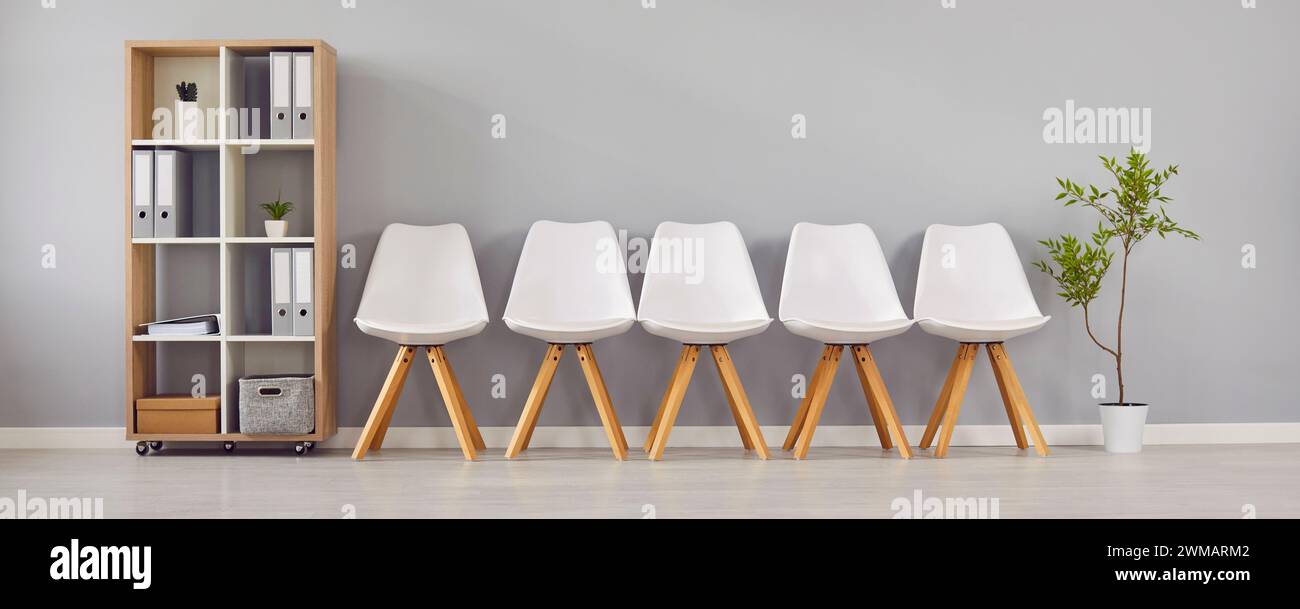 Salle d'attente avec une rangée de chaises, une étagère et une plante verte dans un bureau d'affaires moderne Banque D'Images