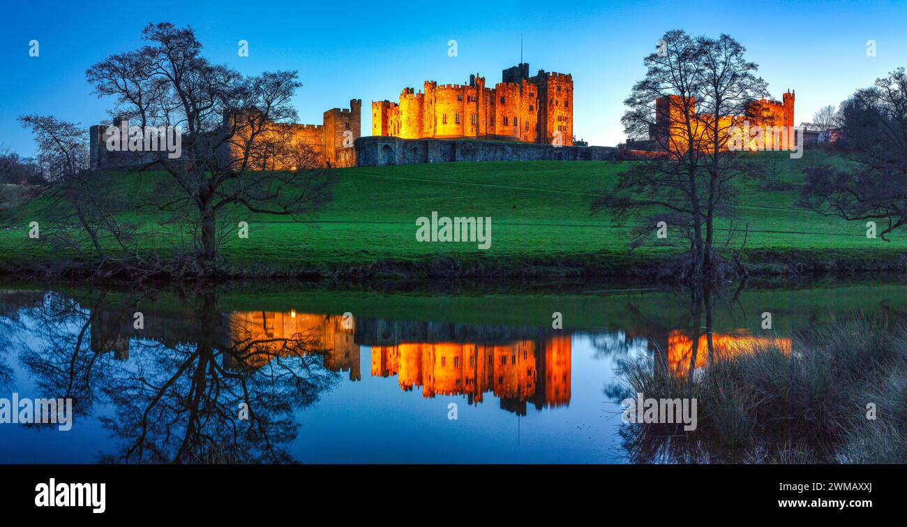 Vue du château d'Alnwick dans le Northumberland inondé la nuit alors que reflété dans la rivière ALN comme vu des pâturages Banque D'Images