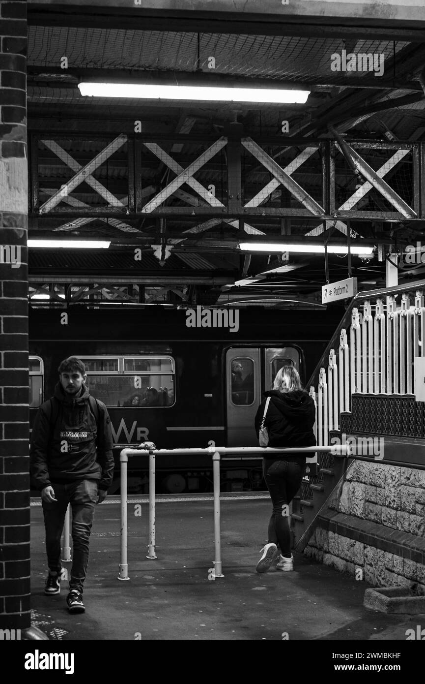 La sortie au quai 1 de la gare de Teignmouth avec une femme blonde attendant et un homme sortant alors que le train est à l'arrêt avec des passagers. Banque D'Images