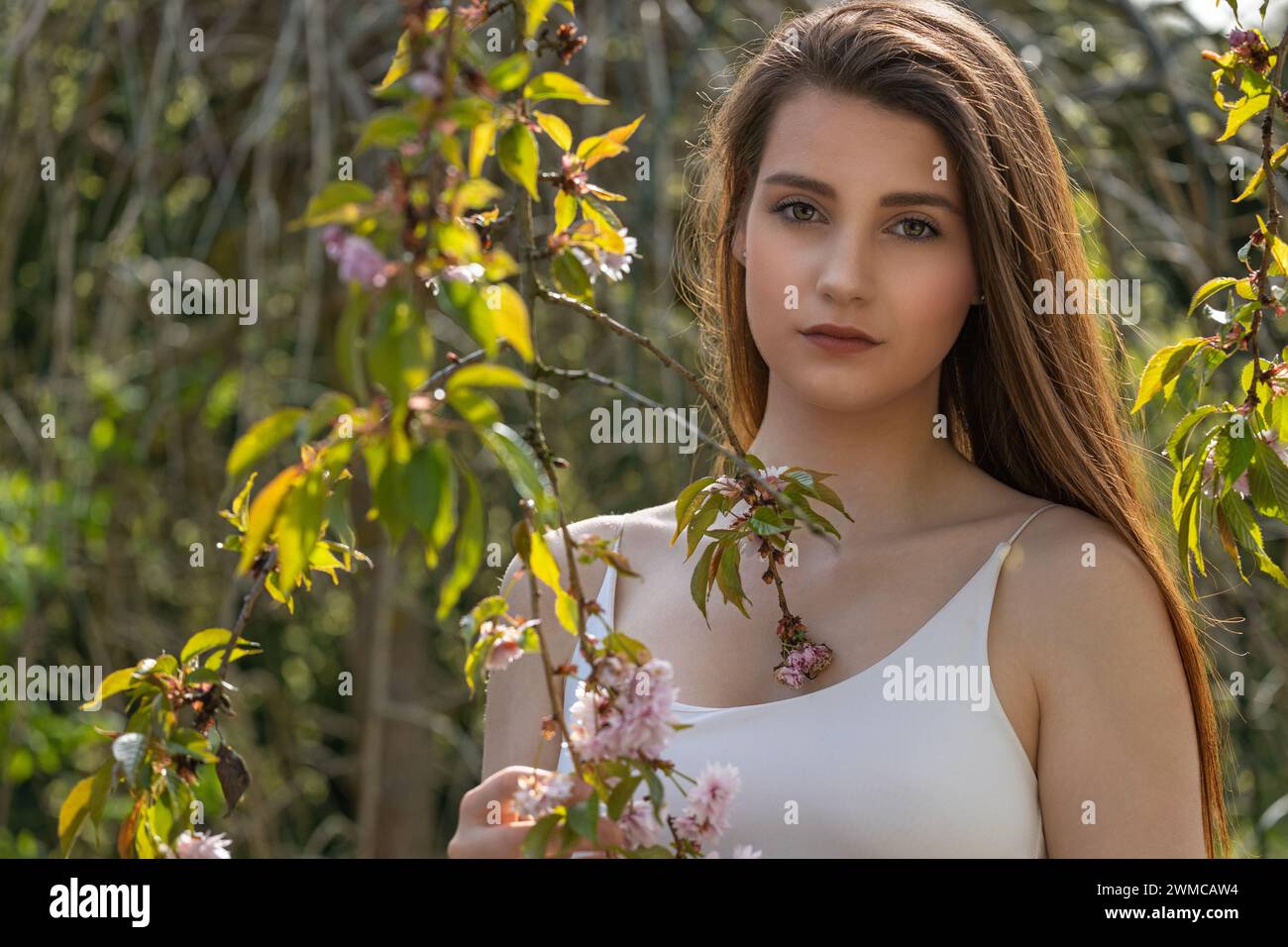 Cool Brunette Girl pose sur la caméra à l'extérieur près de l'arbre sakura. Horizontalement. Banque D'Images