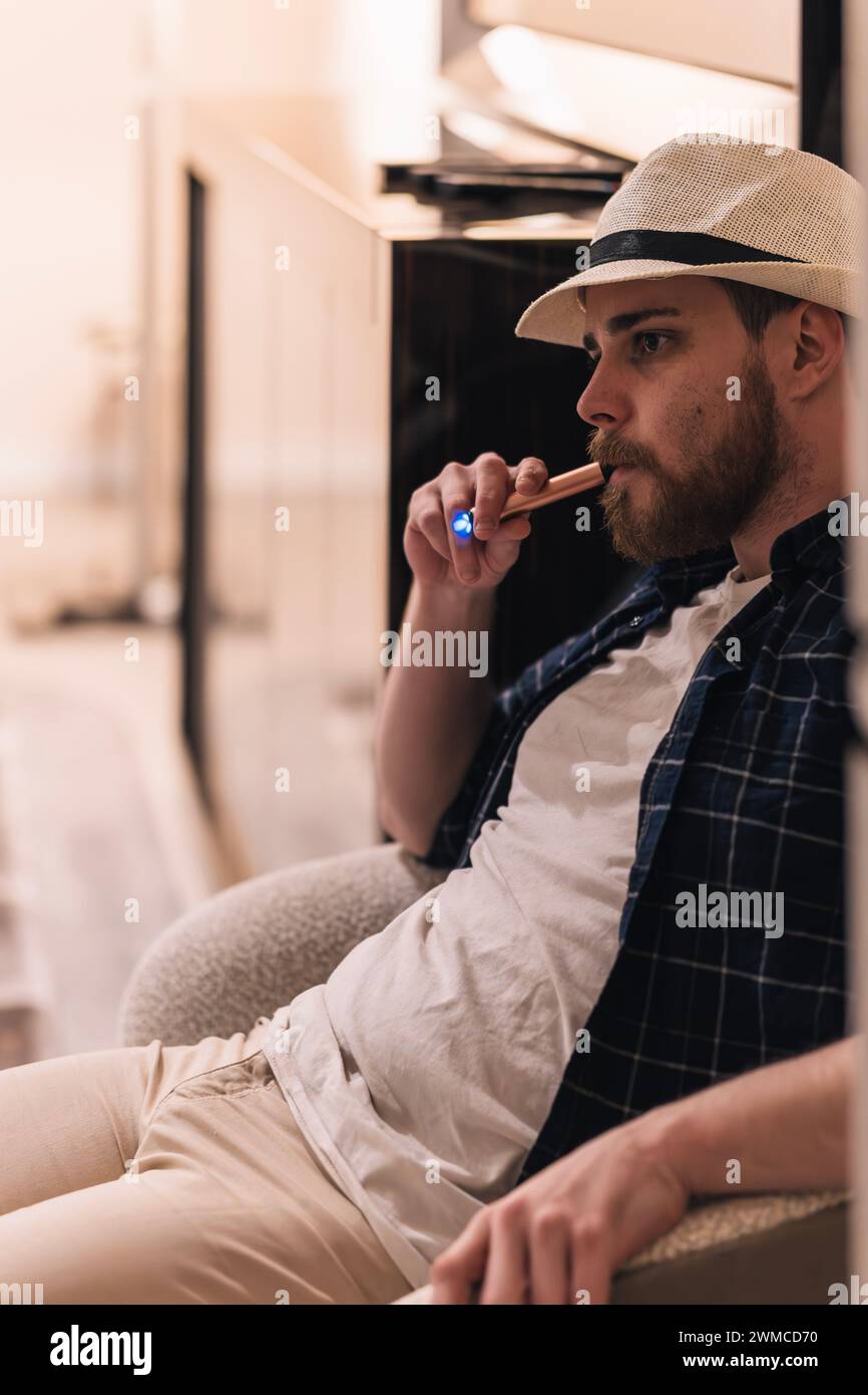 Portrait d'un homme fumant de la vape sur le canapé de son salon. Concept de style de vie Banque D'Images