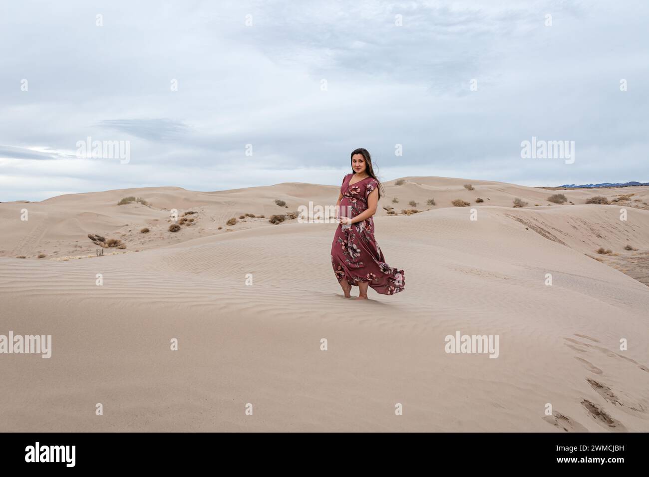 Femme enceinte dans une longue robe debout sur une dune de sable, Utah, USA Banque D'Images