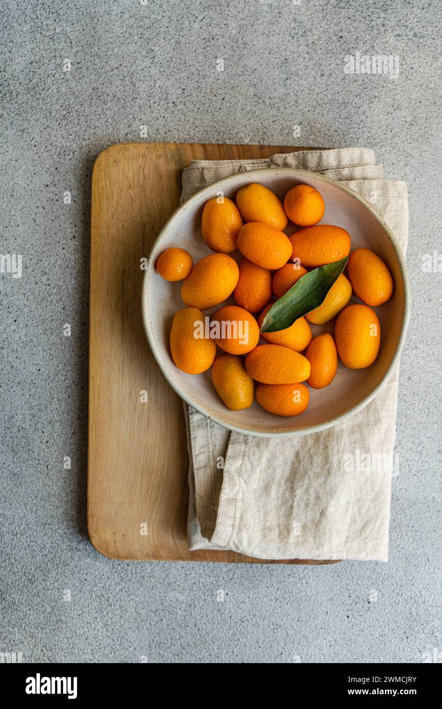 Vue aérienne de kumquats mûrs dans un bol sur une serviette pliée et planche à découper Banque D'Images