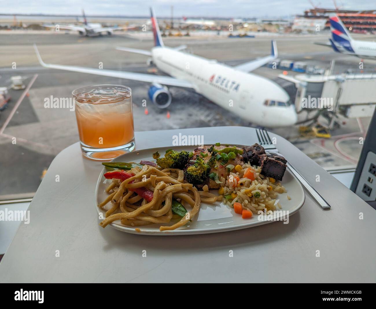 New York City, NY - 21 février 2024 : cuisine asiatique et une boisson dans un salon Delta avec un avion au loin Banque D'Images