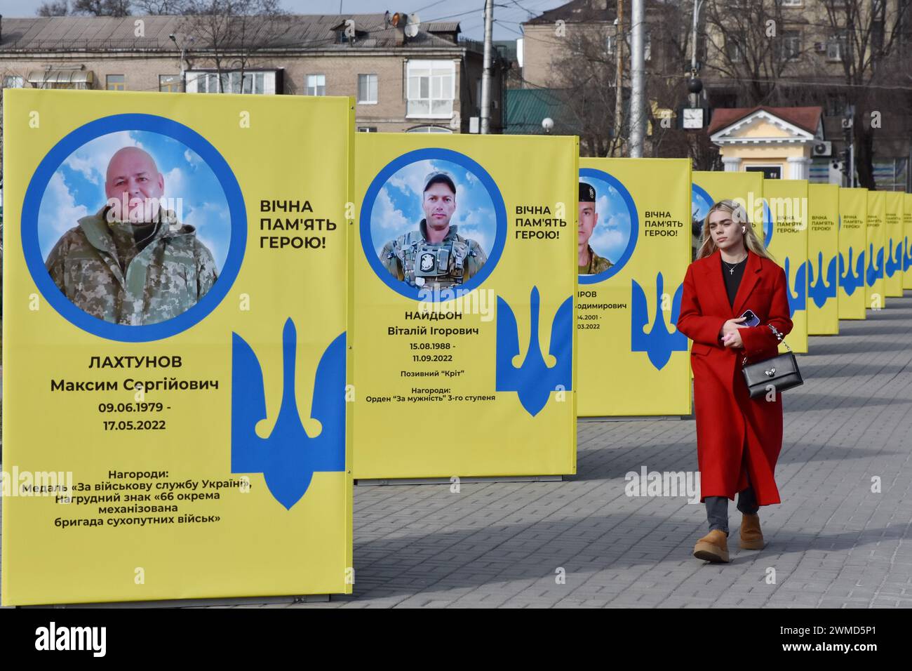 Une femme passe devant des stands de portraits de soldats ukrainiens tombés au combat dans le centre de Zaporizhzhia. Le président ukrainien Volodymyr Zelensky a marqué le deuxième anniversaire de l'invasion russe en déclarant que son pays "réussira". L'Ukraine a défié les prédictions de combattre la Russie, mais il y a des signes que la guerre tourne en faveur de la Russie. Le gouvernement ukrainien a cessé de partager le nombre de ses militaires morts il y a longtemps. Mais le nombre toujours croissant de tombes fraîches, des deux côtés des lignes de front, dresse un tableau douloureusement clair. Banque D'Images
