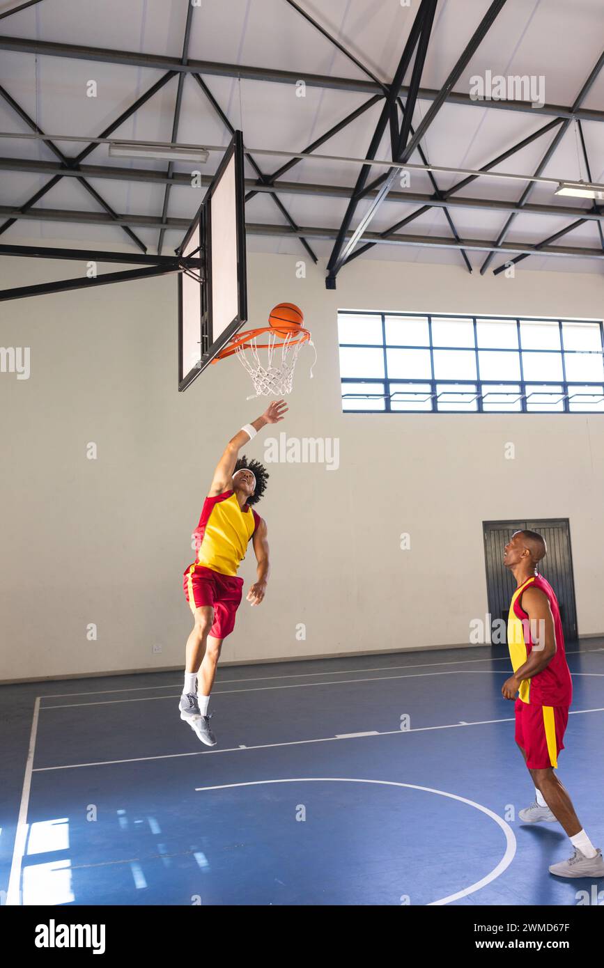 Jeune homme biracial saute pour un tir de basket-ball dans une salle de gym intérieure, avec espace de copie Banque D'Images