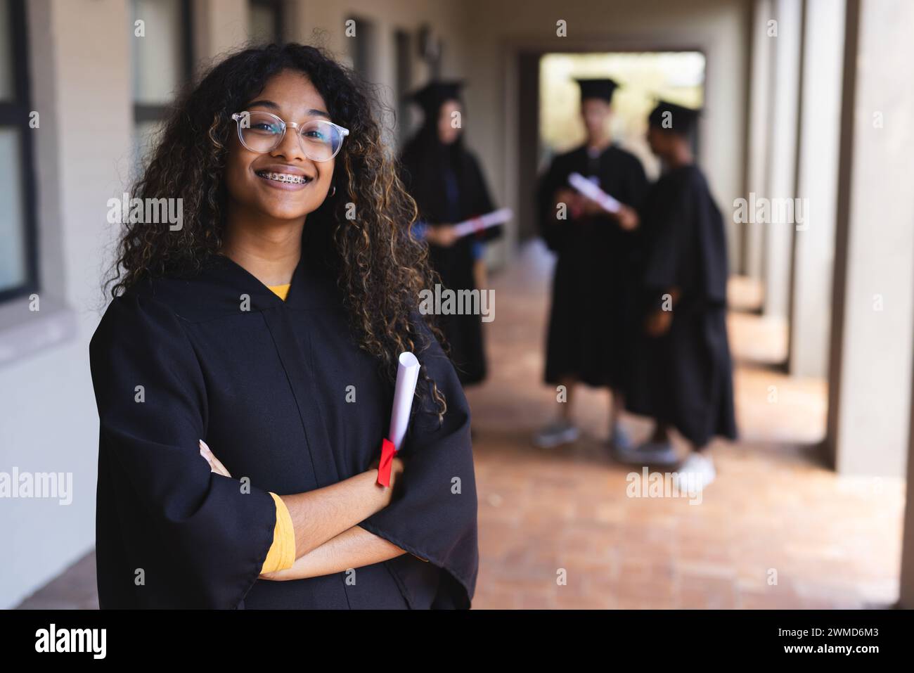 Fier diplômé en casquette et robe détenant un diplôme à l'école secondaire Banque D'Images
