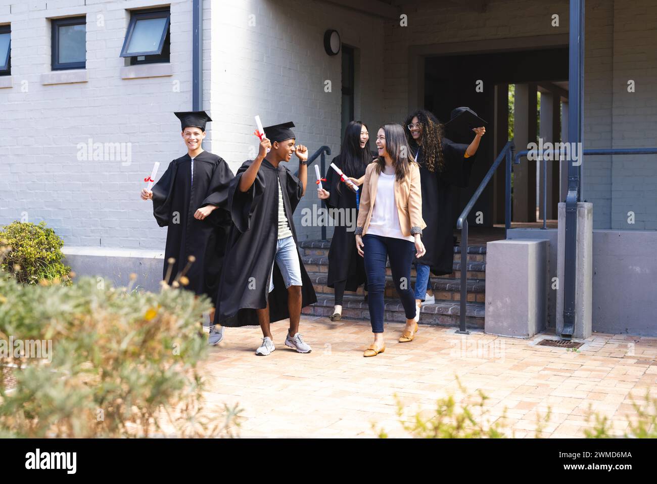 Divers étudiants célèbrent la remise des diplômes à l'extérieur d'un bâtiment d'école secondaire Banque D'Images