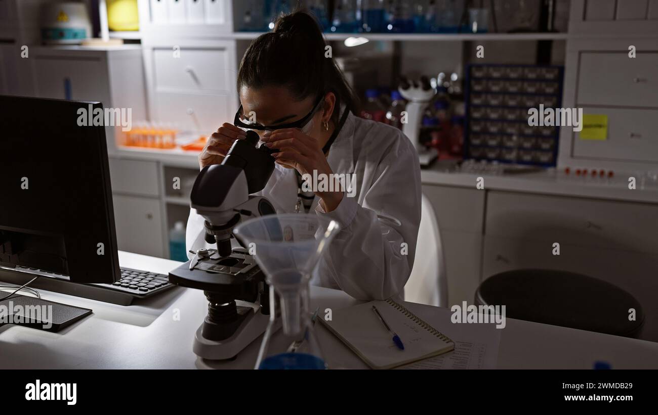 Immergé dans la découverte, belle jeune scientifique hispanique travaillant tard la nuit au laboratoire, absorbé dans la recherche médicale, expérimentant avec la cuve d'essai Banque D'Images