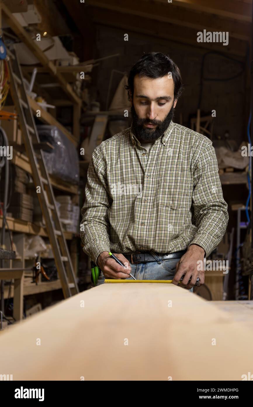 Photo verticale un menuisier concentré mesure méticuleusement une planche de bois, assurant la précision pour son prochain projet créatif de menuiserie. Concept commercial Banque D'Images