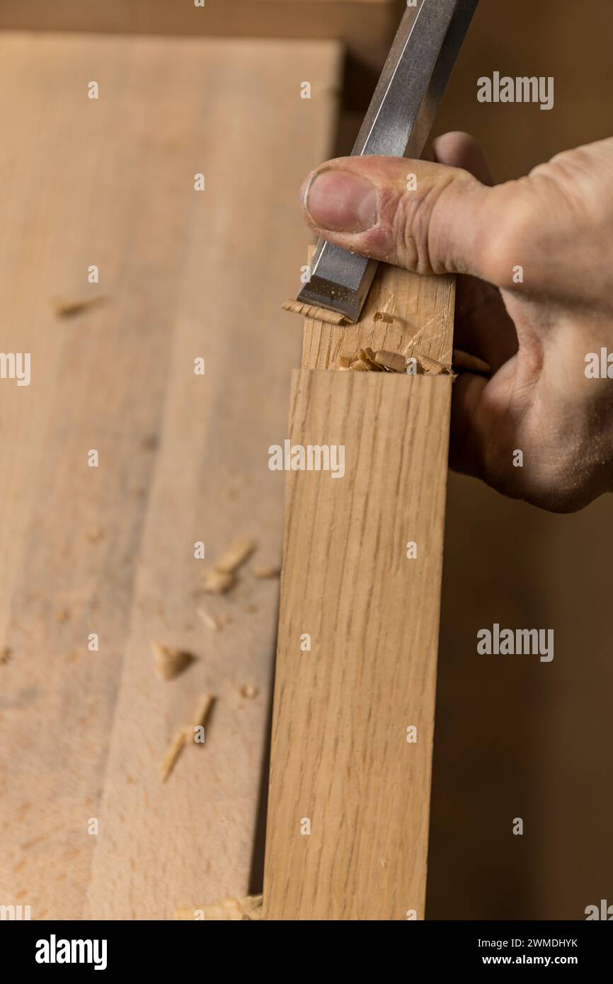Photo verticale la photo se concentre sur le mouvement précis de la main d'un charpentier tout en ciselant une encoche dans une planche de bois, avec des copeaux de bois dispersés autour. C Banque D'Images