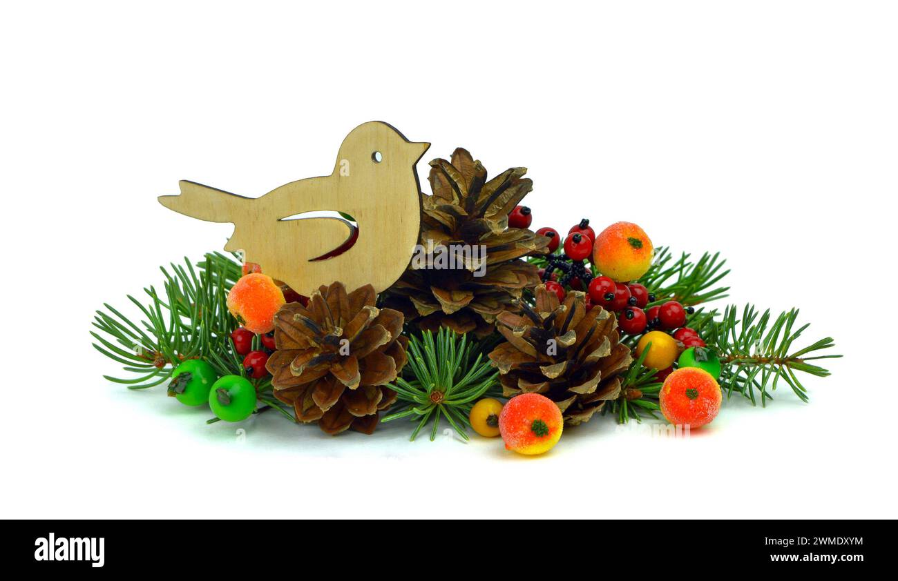 Arrangement de Noël. Petit oiseau en bois fait à la main se trouve sur les branches d'un arbre de Noël, des cônes, des baies décoratives colorées. Isolation sur un blanc Banque D'Images