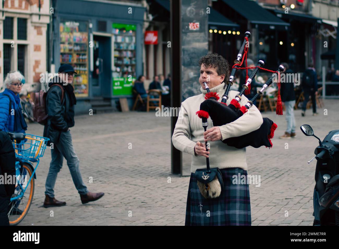 Gand, Belgique - janvier 31 2024 : iper dans la tenue traditionnelle écossaise joue sur la cornemuse dans la ville de gent avec les gens et les touristes qui le regardent Banque D'Images