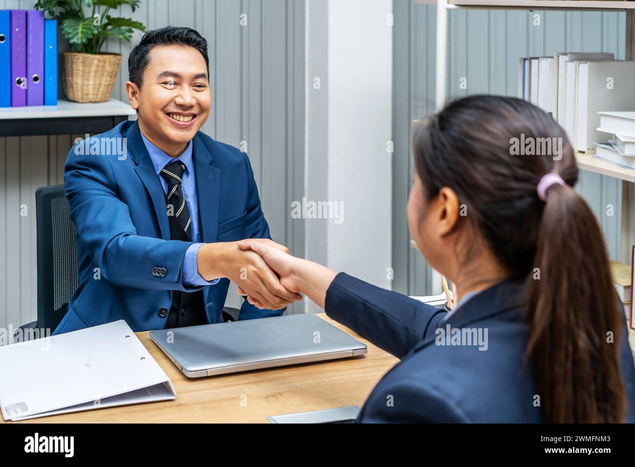 Un jeune homme et une jeune femme se serrent la main à un bureau en accord Banque D'Images