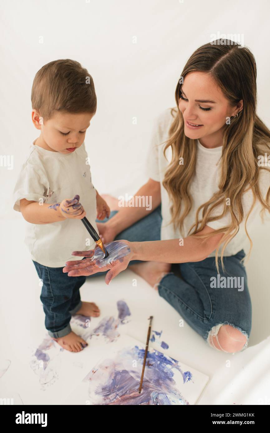 Jeune enfant peignant la main de maman souriante pour créer des empreintes de mains sur toile Banque D'Images