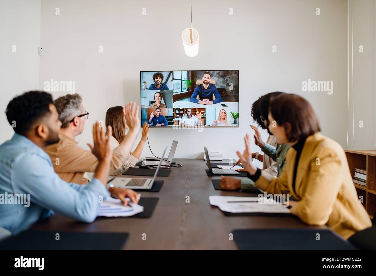 Une équipe diversifiée de professionnels participe avec enthousiasme à une visioconférence, agitant la main, reflétant une culture d'entreprise chaleureuse et inclusive qui embrasse la collaboration à distance et l'unité d'équipe Banque D'Images