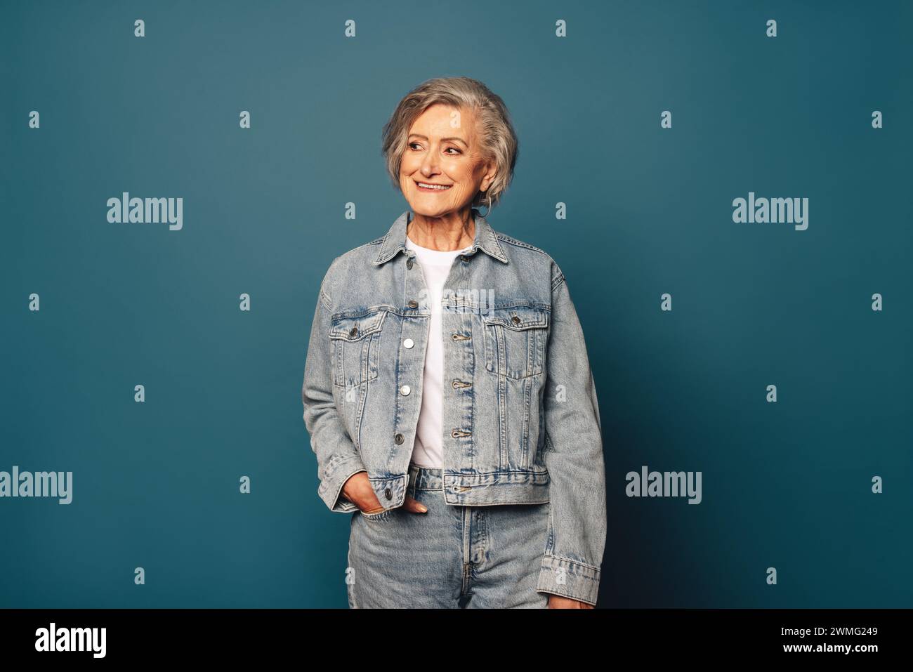 Femme âgée confiante et joyeuse en Jean denim décontracté et vêtements sur fond bleu. Avec une expression réfléchie et pensive, elle semble mature y Banque D'Images