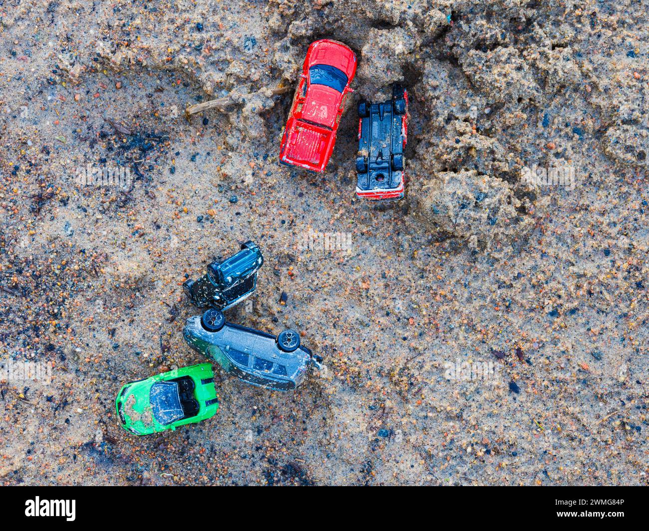 Une variété de voitures jouets colorées est dispersée sur une surface graveleuse et sablonneuse, suggérant une activité ludique. Le cliché, pris d'en haut, capture l'information Banque D'Images