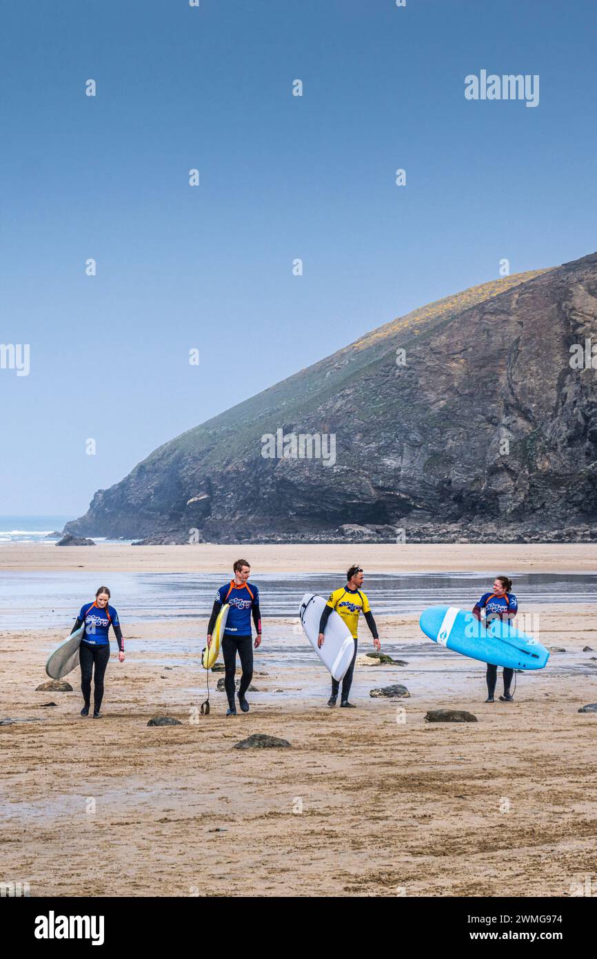 Trois surfeurs novices et leur instructeur de surf portant leurs planches de surf après une leçon de surf à Mawgan Porth à Cornwall au Royaume-Uni. Banque D'Images