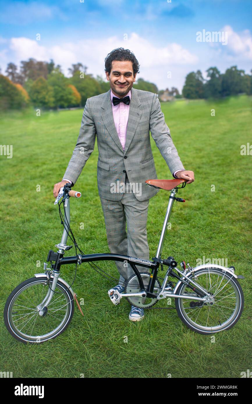 Jeune homme avec noeud papillon tenant un vélo pliant Brompton dans le parc. Banque D'Images