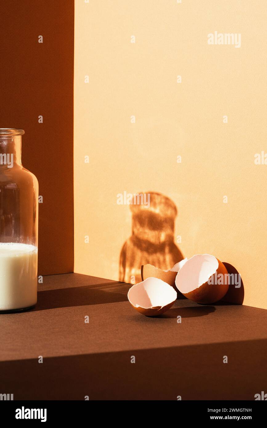 Coquille d'oeuf vide cassée sur coquille d'oeuf brun et beige avec une bouteille de lait, tons chauds, studio tourné avec des ombres nettes et un contraste élevé Banque D'Images