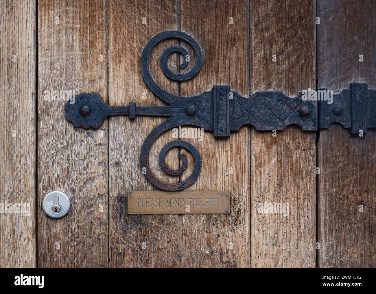 Ferronnerie à charnière et panneau « Please Mind the Step » sur une porte en bois rustique à l'Université d'Oxford, Oxford, Angleterre, Royaume-Uni. Banque D'Images