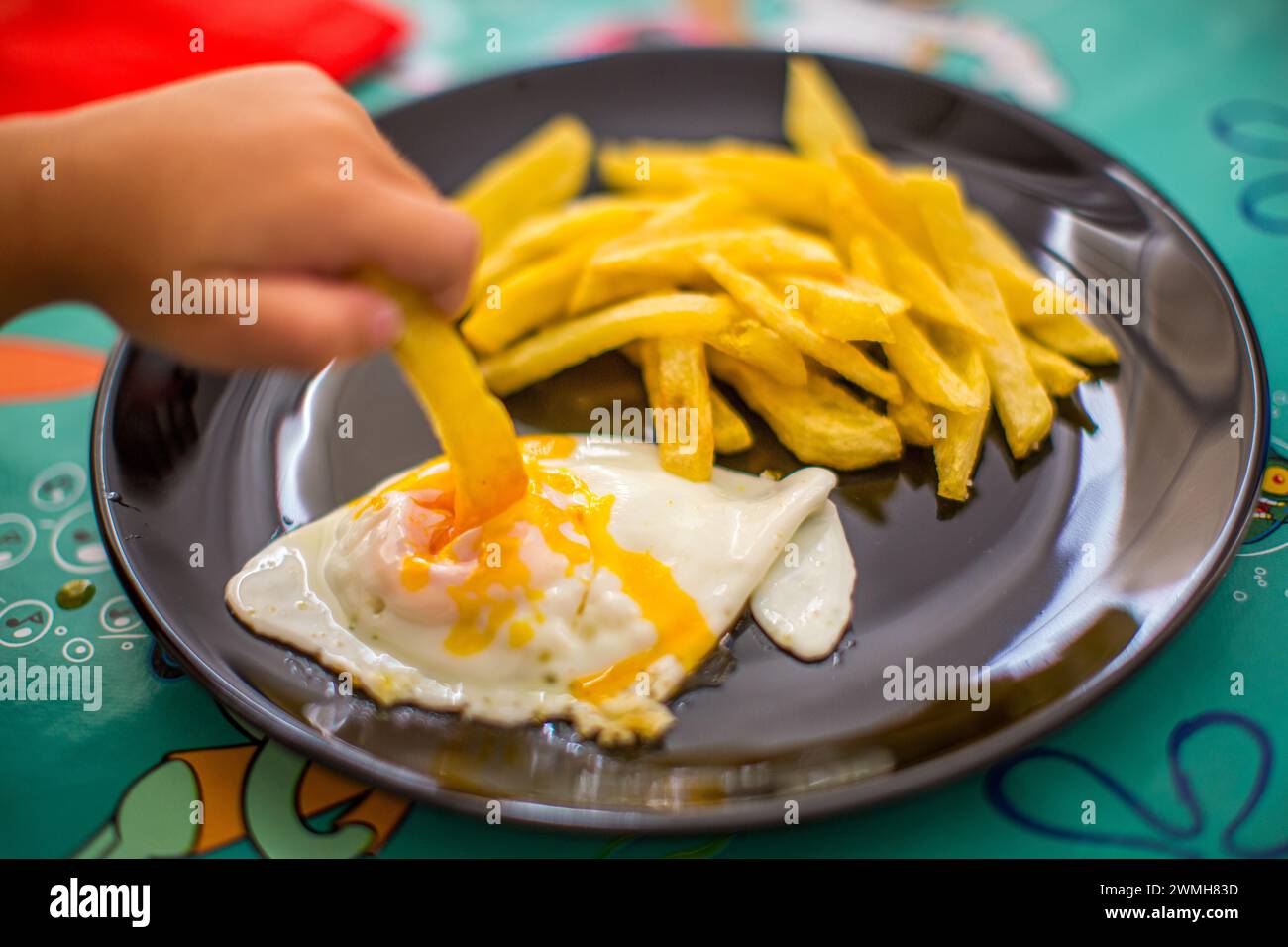 Une main d'enfant saisissant une frite à côté d'un œuf ensoleillé. Banque D'Images