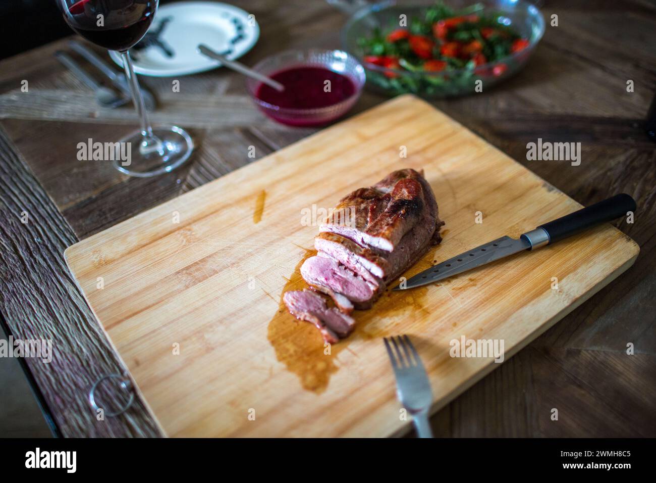 Une longe de porc rôtie juteuse tranchée sur une planche à découper à côté d'un verre de vin rouge. Banque D'Images