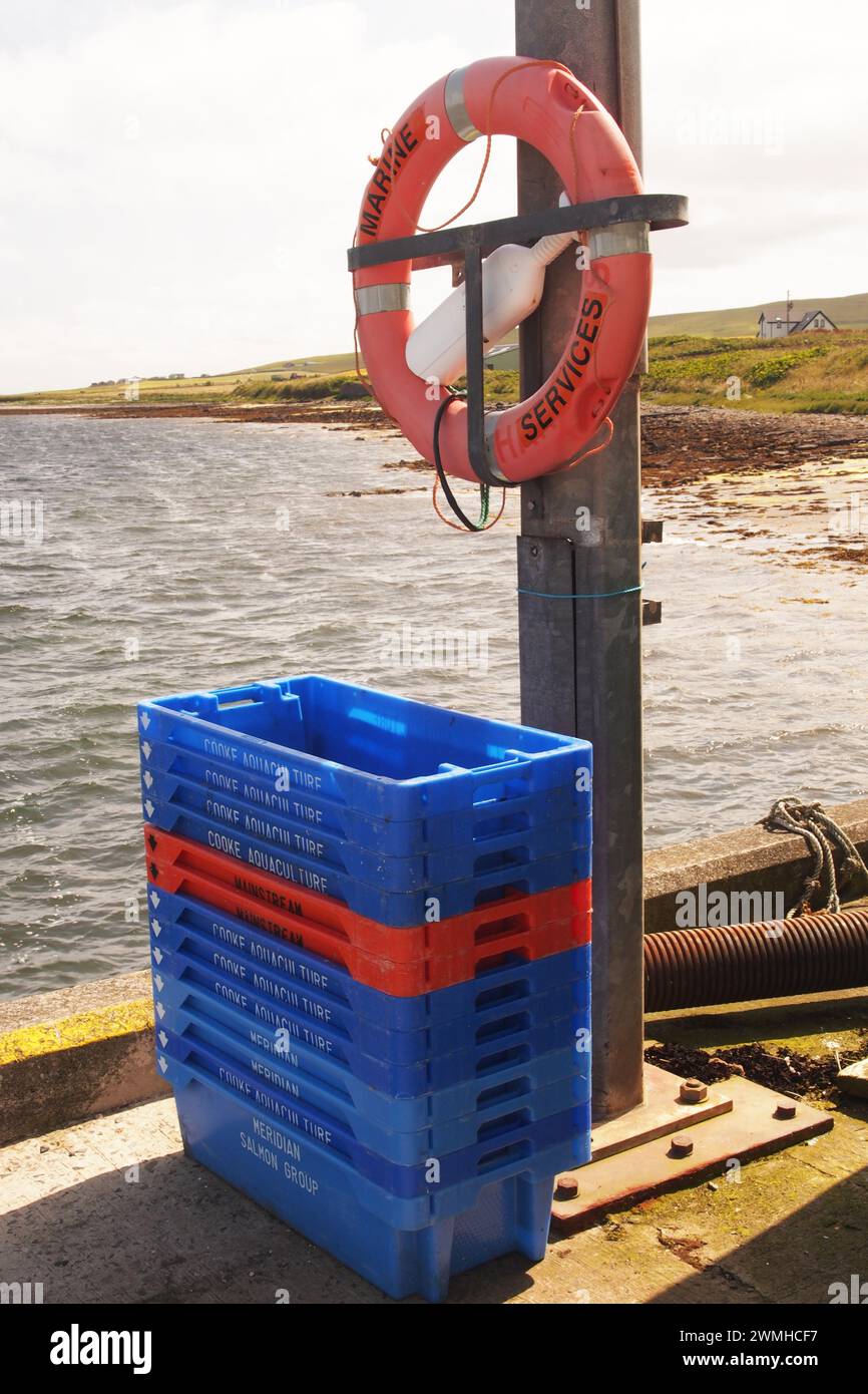 Une ceinture de sauvetage sur un poteau avec une pile de boîtes de pêche devant sur la jetée de Tingwall, Orcades, Écosse, Royaume-Uni Banque D'Images