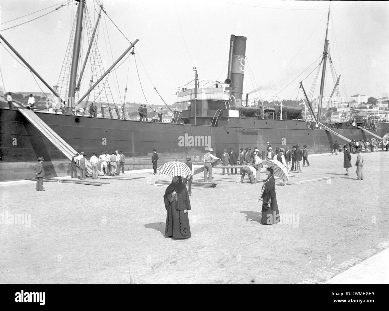 Un groupe d'hommes et de femmes marche à côté d'un grand navire dans un port du sud-est. Début du XXe siècle. Vieille photographie numérisée à partir d'une plaque de verre. Banque D'Images