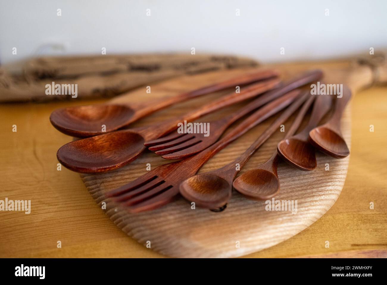 Un ensemble de cuillères et fourchettes en bois fabriquées à la main repose sur une planche de bois. La riche couleur acajou des ustensiles ajoute de la chaleur à l'atmosphère de la cuisine. Banque D'Images