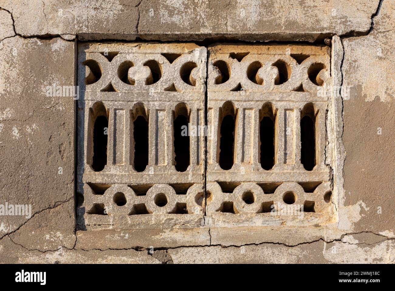 Vieille fenêtre sculptée en pierre de style arabe avec mur de pierre fissuré autour dans le village abandonné d'Al Jazirah Al Hamra à Ras Al Khaimah, Émirats arabes Unis. Banque D'Images