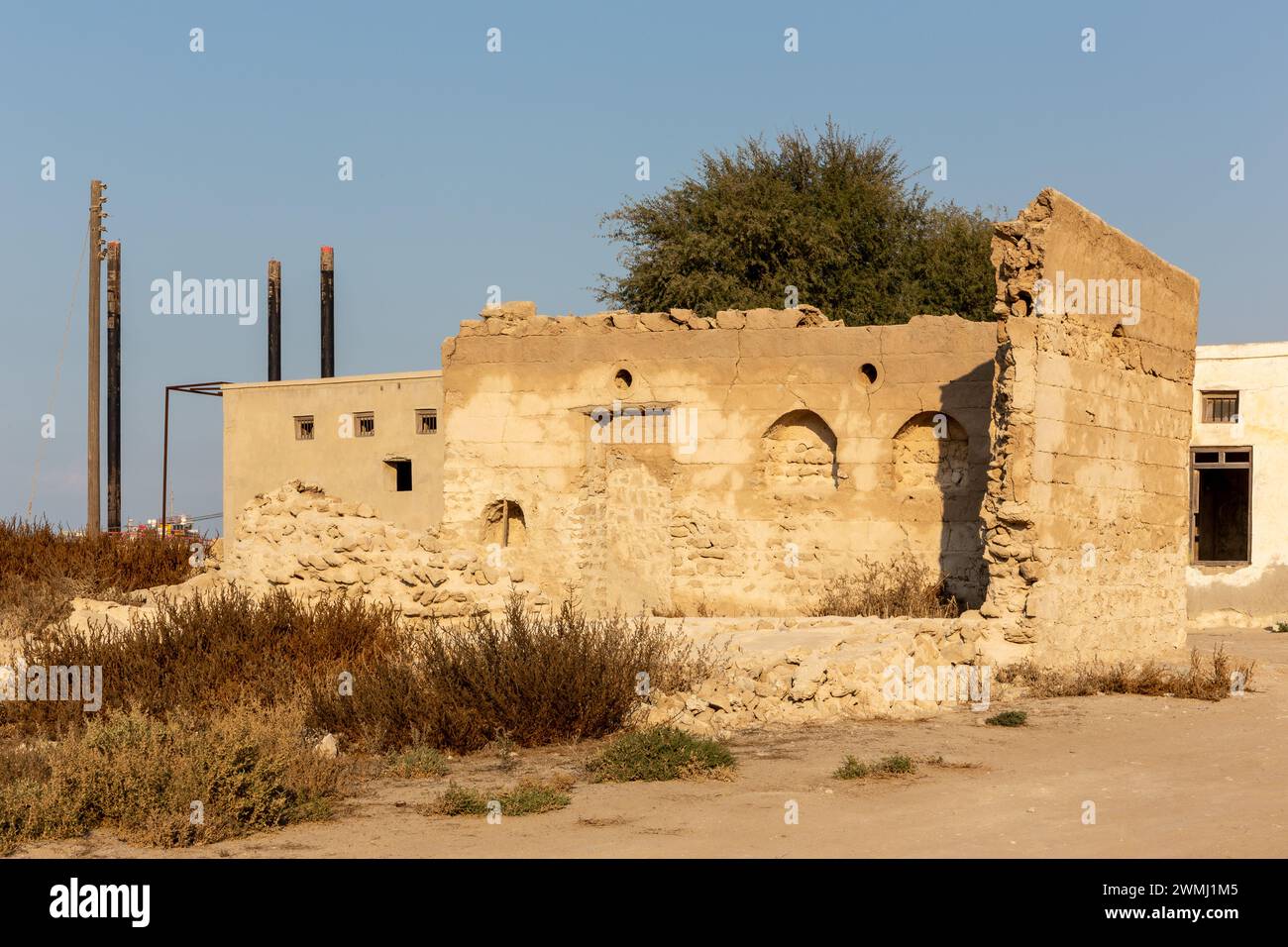 Mur de bâtiment résidentiel en ruine avec des fenêtres en arc de style arabe dans la ville hantée d'Al Jazirah Al Hamra à Ras Al Khaimah, Émirats arabes Unis. Banque D'Images