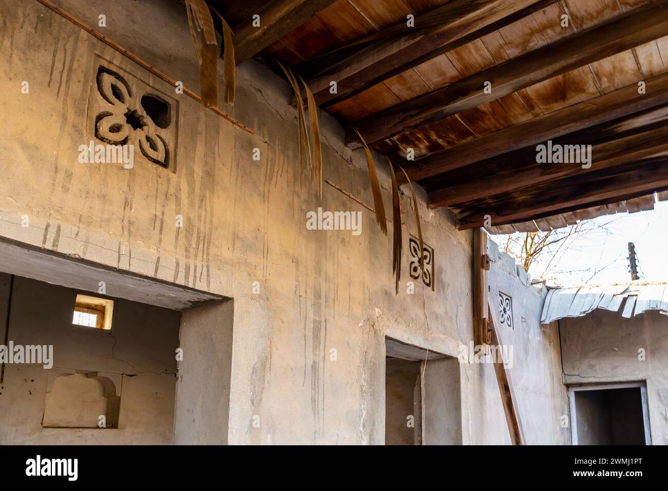 Mur de bâtiment résidentiel en ruine avec des ornements de fleurs arabes sculptées et toit de chaume traditionnel fait de branches de palmier à Jazirah Al Hamra, Émirats arabes Unis Banque D'Images
