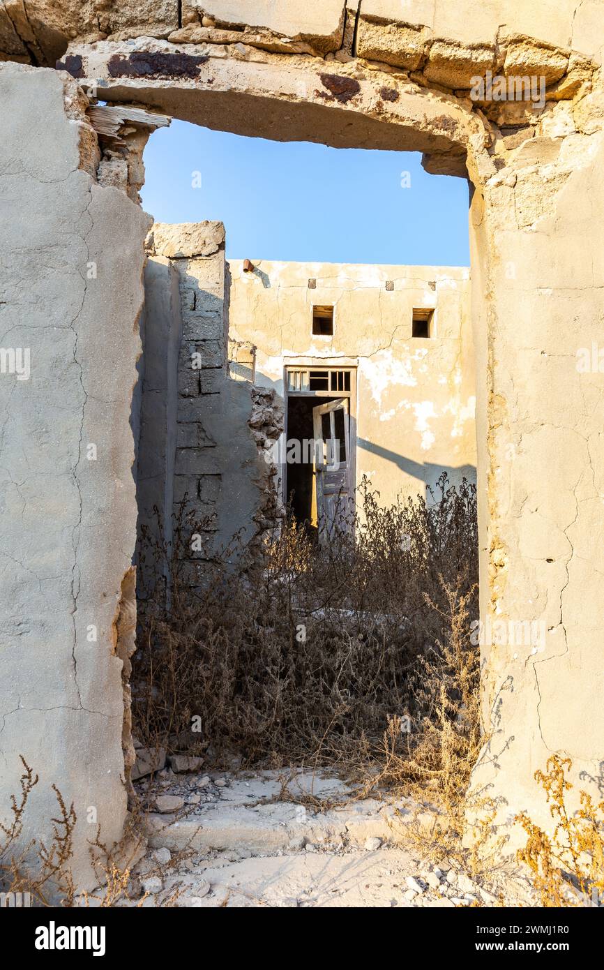 Bâtiments résidentiels en ruine, murs de briques démolis et cour couverte de végétation dans la ville hantée d'Al Jazirah Al Hamra à Ras Al Khaimah (Émirat arabe Uni) Banque D'Images