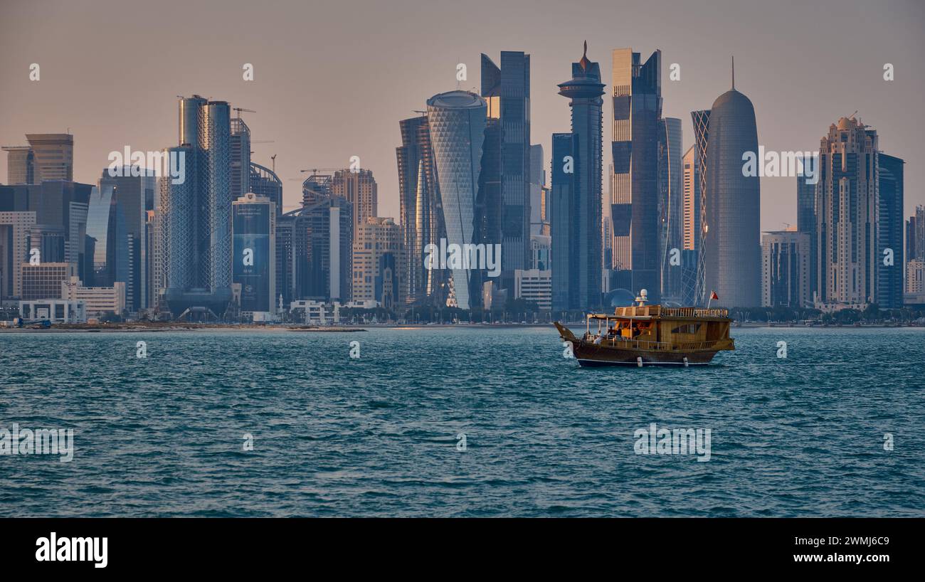 Doha, Qatar skyline de la rue corniche au coucher du soleil avec des boudins et des bateaux dans le golfe arabe Banque D'Images