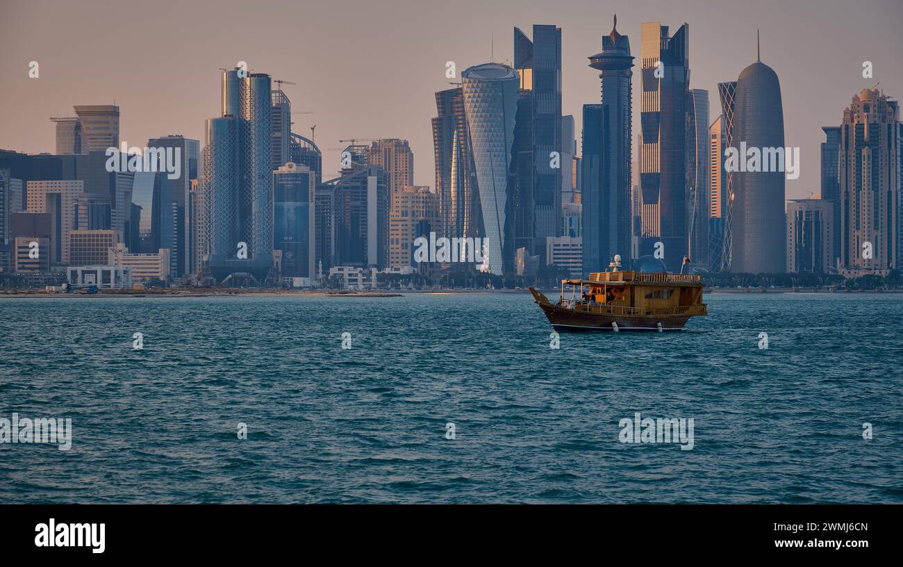 Doha, Qatar skyline de la rue corniche au coucher du soleil avec des boudins et des bateaux dans le golfe arabe Banque D'Images