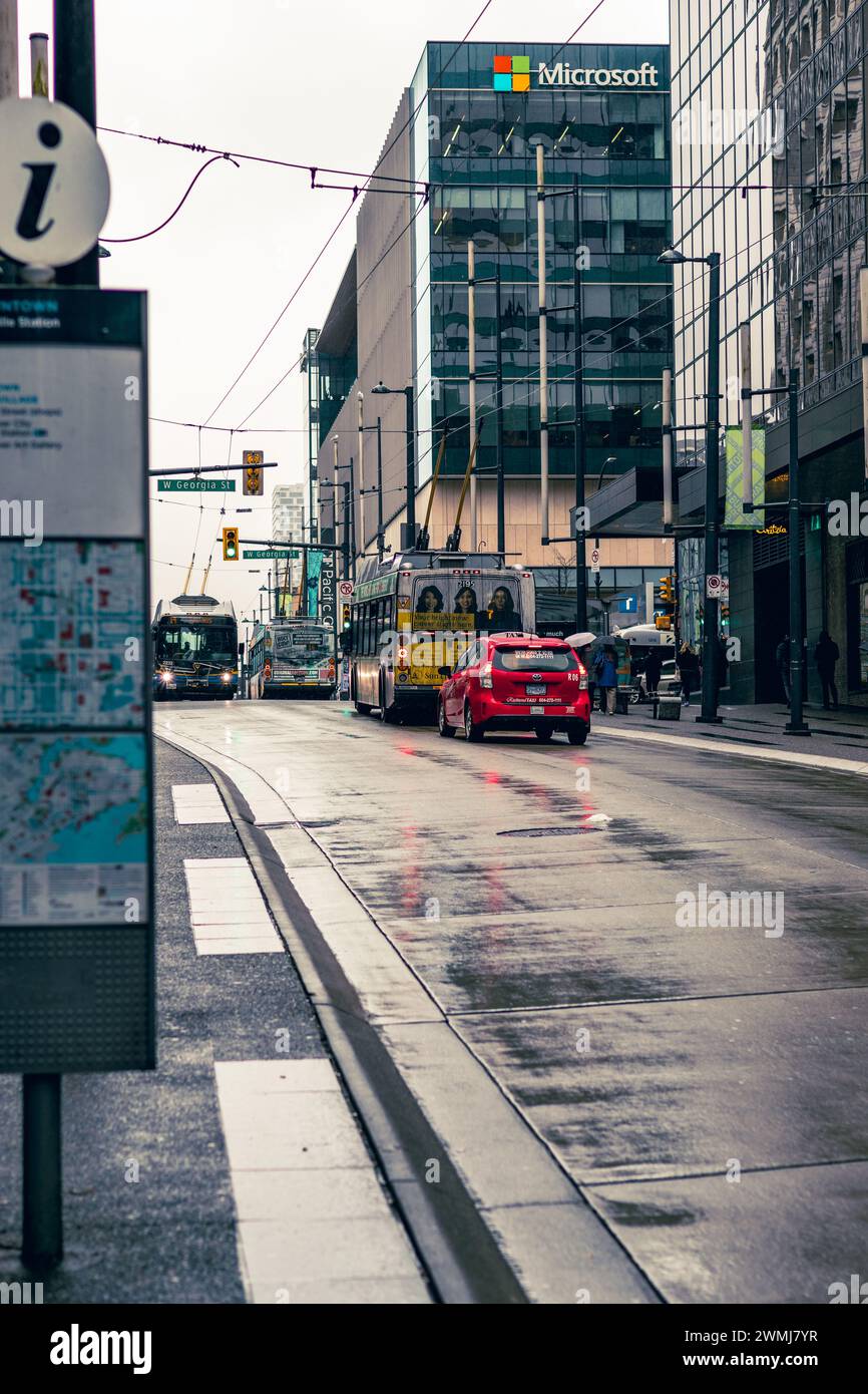 Vancouver, Canada - 21 février 2024 : une vue de Granville Street un jour de pluie, montrant un taxi rouge vif derrière un bus, attendant de traverser Georgia Street. Banque D'Images