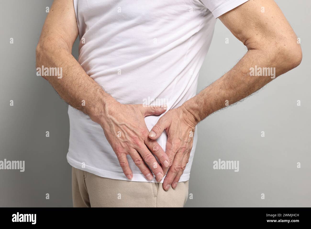 Symptômes de l'arthrite. Homme souffrant de douleurs articulaires de la hanche sur fond gris, gros plan Banque D'Images