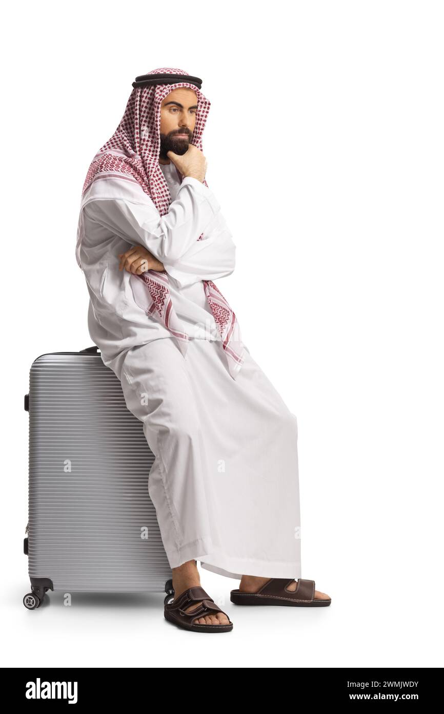 Homme arabe saoudien pensif assis sur une valise isolé sur fond blanc Banque D'Images